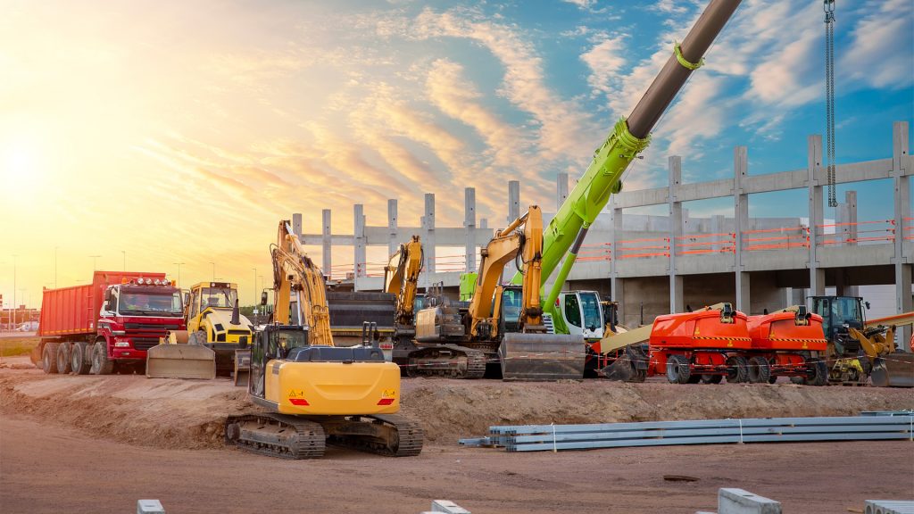 Cantiere edile con macchinari pesanti, tra cui escavatori, gru e camion, utilizzati per il noleggio mezzi in edilizia, ottimizzando costi e produttività