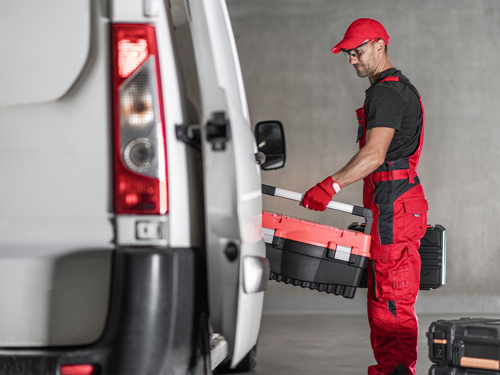 Tecnico al lavoro con attrezzatura di sicurezza vicino a un furgone aziendale, esempio di sicurezza persone durante interventi operativi su strada.